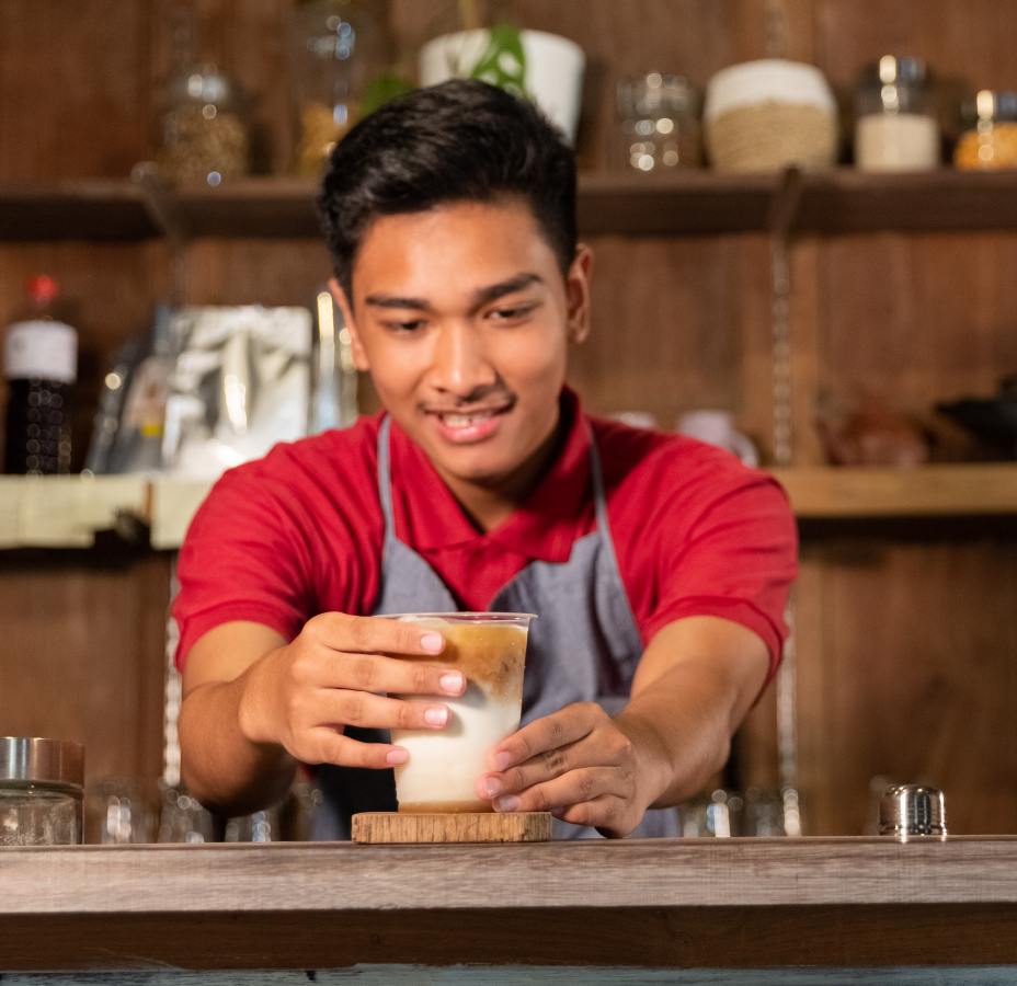 young adult preparing beverage behind counter indo